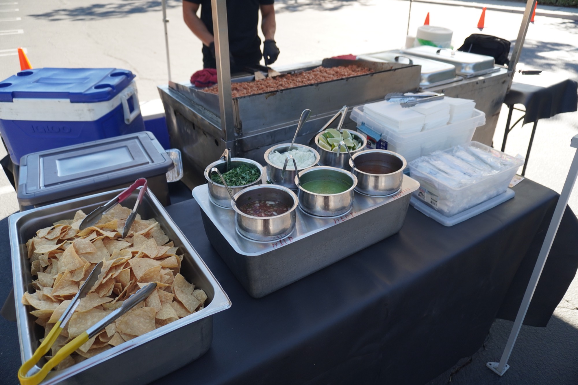 A B&C cook working the cart griddle, with the salsa bar — steel ramekins hand-labelled mild, medium and hot — chips and limes set out along the table
