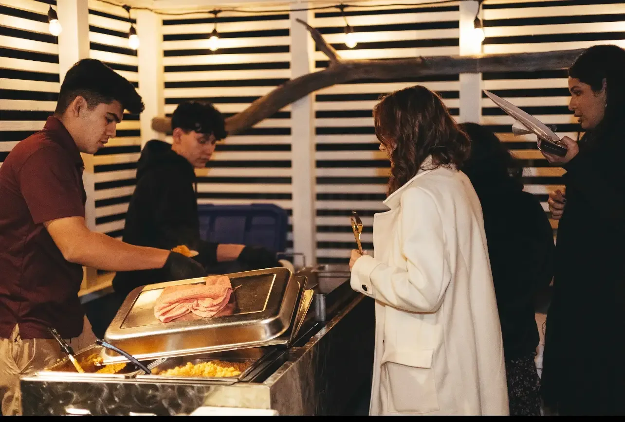 Two B&C servers plating up for guests at an evening party under string lights