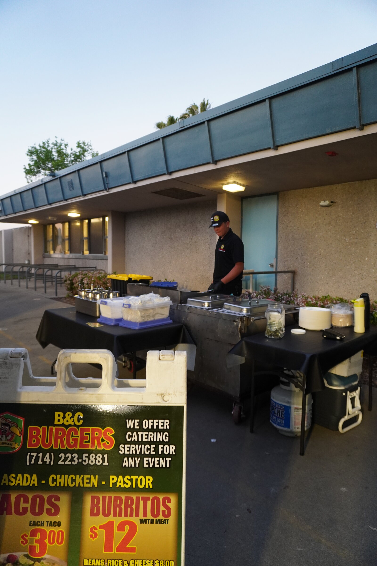 The catering setup outside a venue in the evening, a cook working the line under the lights