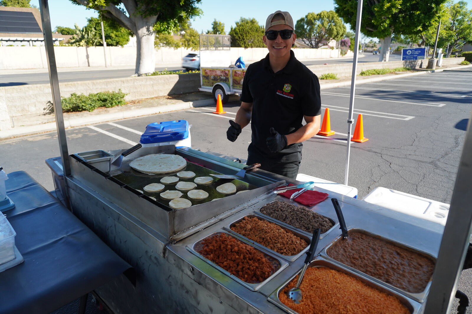 A B&C cook warming tortillas on the cart griddle, with trays of Spanish rice and refried beans alongside
