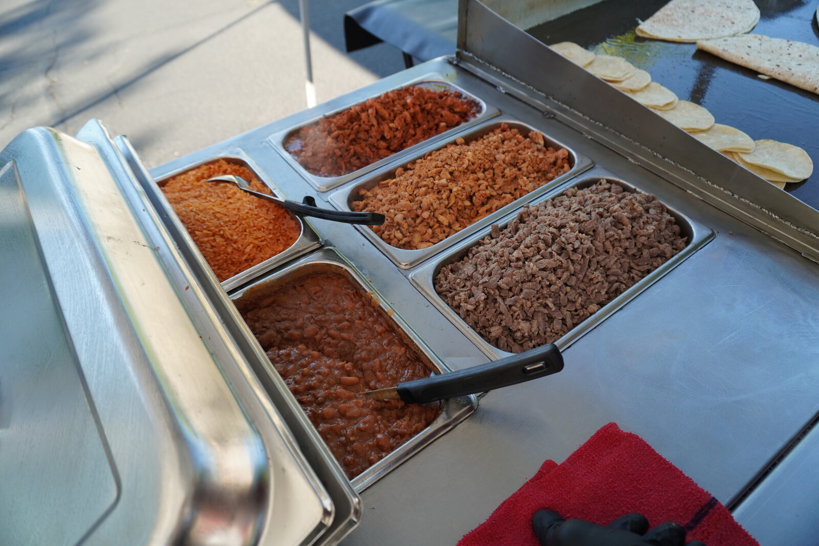 Trays of Spanish rice and refried beans in the cart, tortillas warming behind them