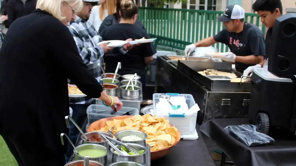Guests plating up along the B&C Burgers taco cart while a cook works the griddle behind the line