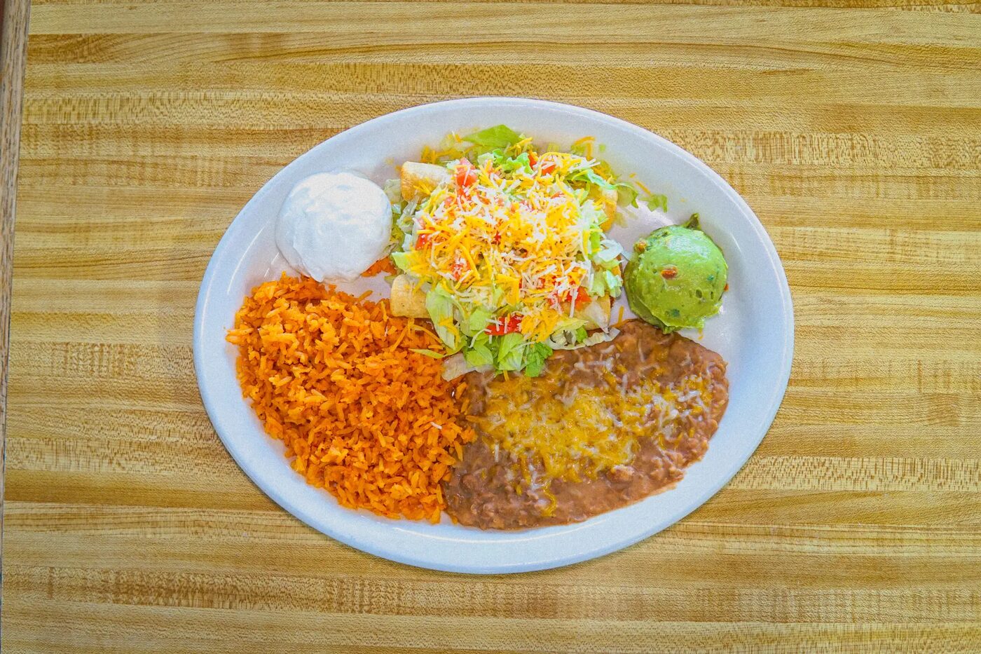 A plate of crisp rolled taquitos with Spanish rice, refried beans, sour cream and guacamole
