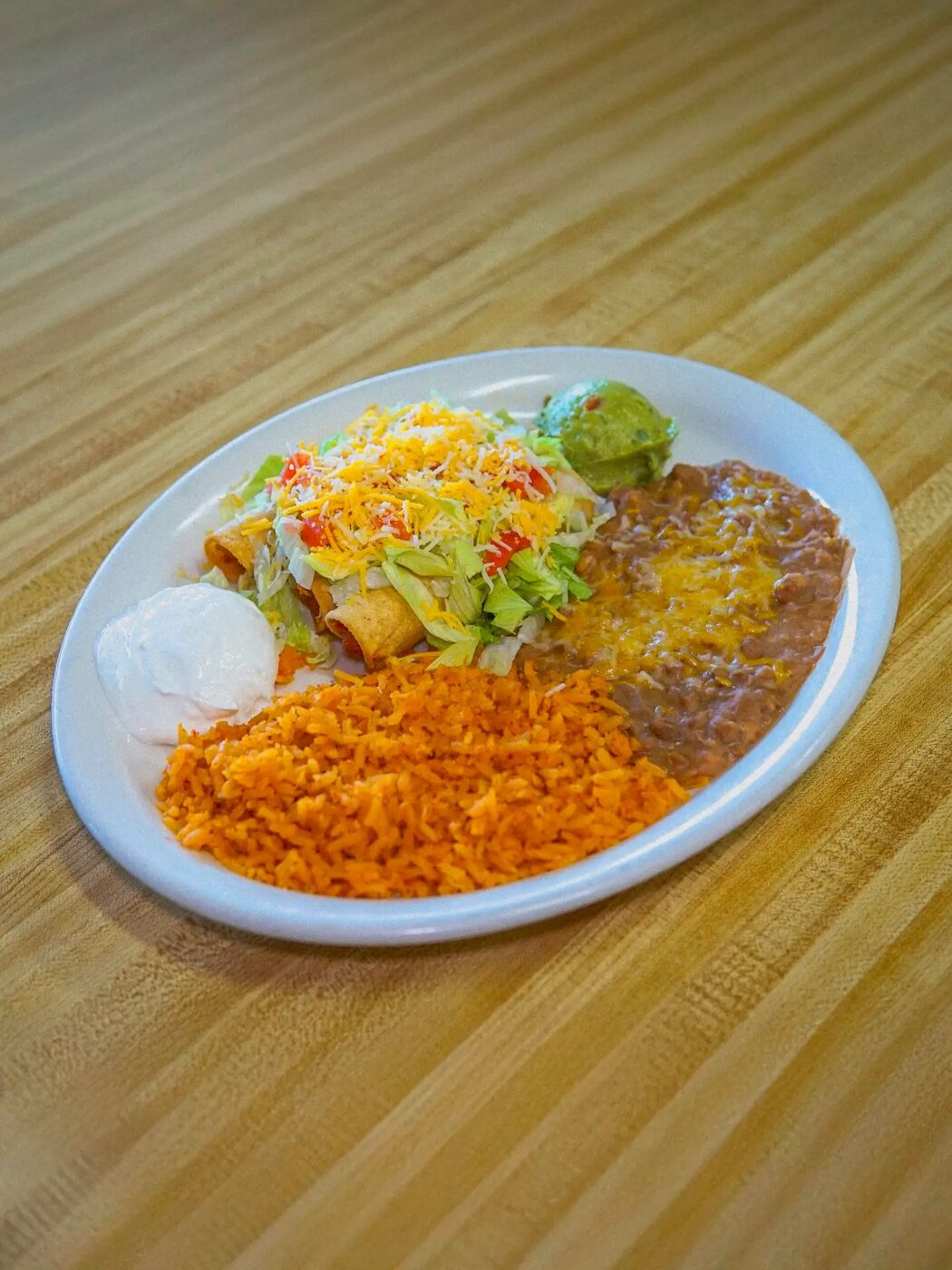 Crisp rolled taquitos under lettuce, tomato and cheese, plated with rice and beans