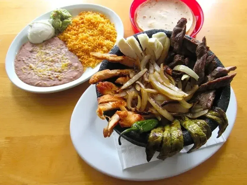 A molcajete of chicken and asada with grilled onion, nopales and panela