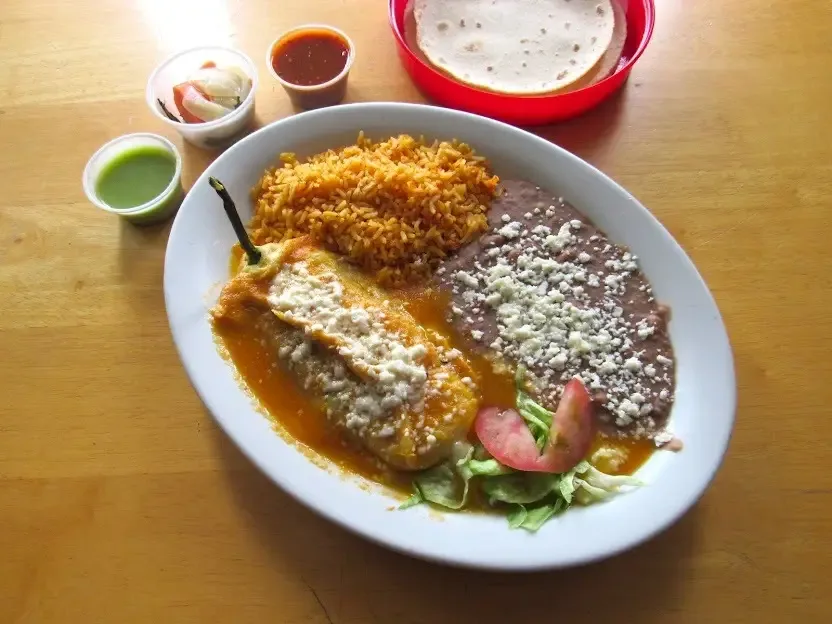 Chile relleno covered in sauce with a side of Spanish rice