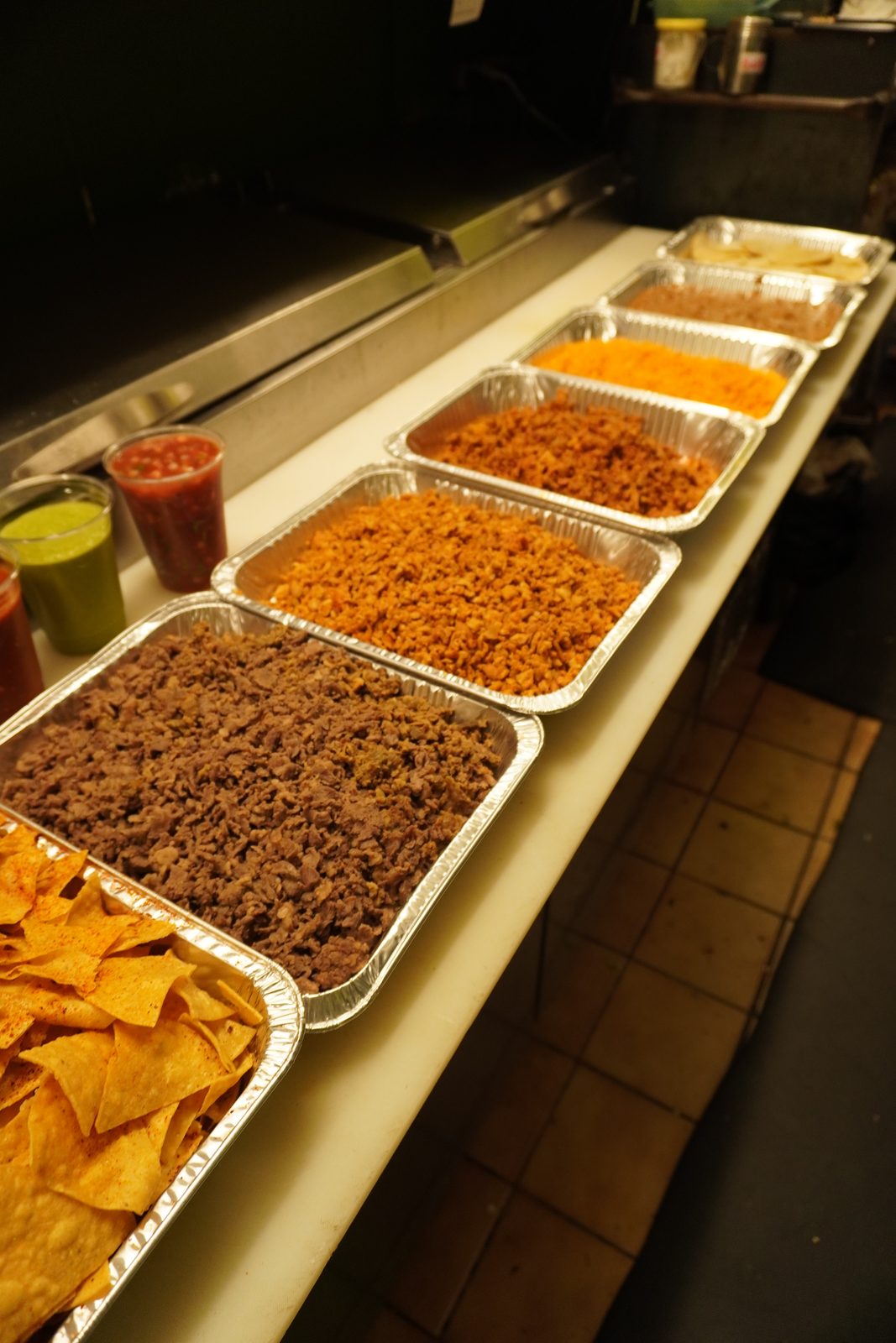 The same line of trays seen low and close, chips in front and salsas alongside