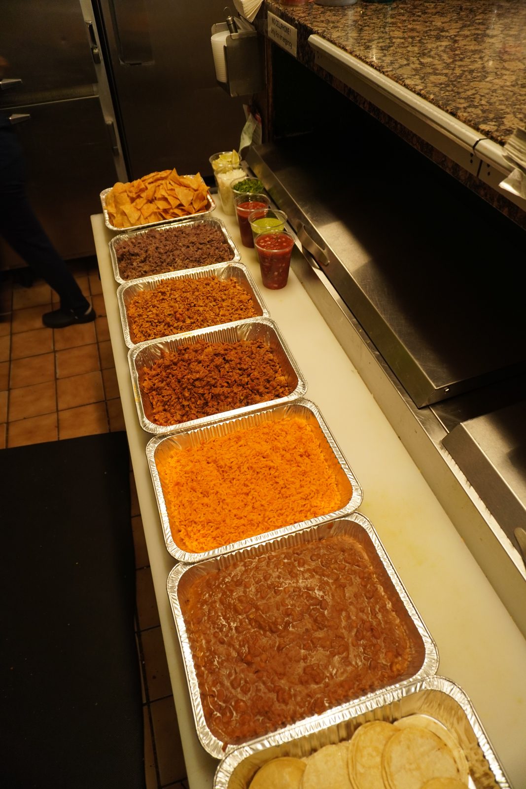 The trays from above, with salsas, chopped onion, cilantro and lime wedges cupped beside them