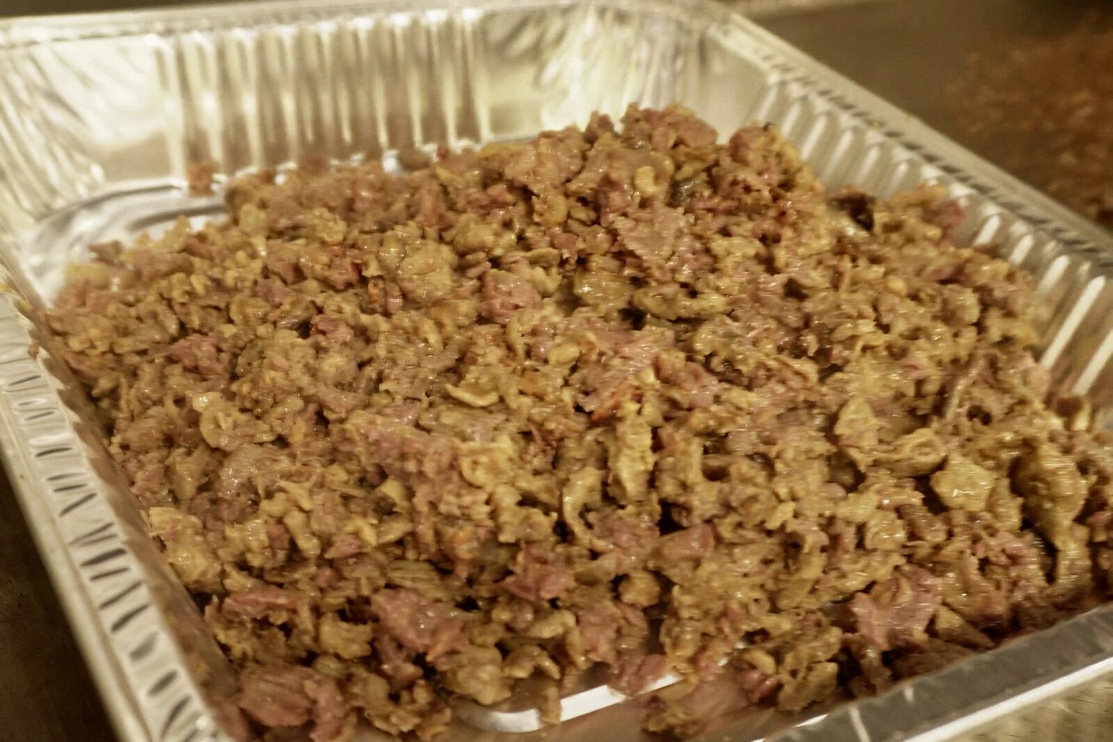 A foil tray filled to the edges with chopped grilled meat